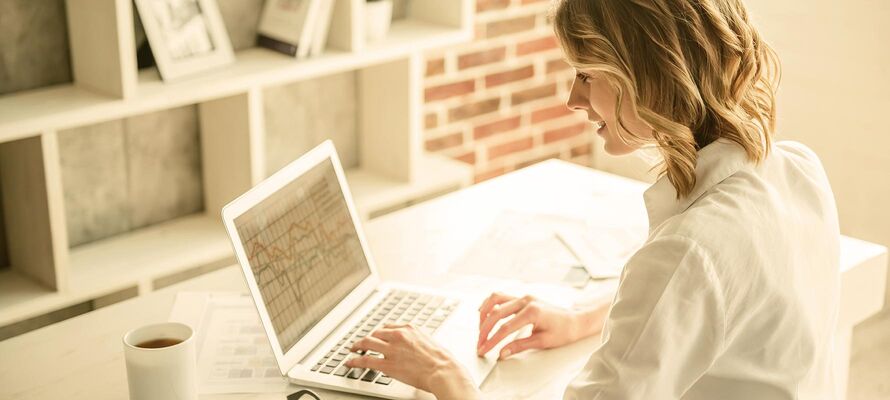 Frau sitzt an ihrem Schreibtisch und arbeitet an ihrem Laptop.